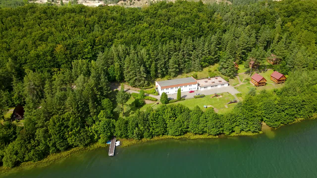 Luftfoto af campingområde ved flodbredden med flere hytter omgivet af blandet grøn skov