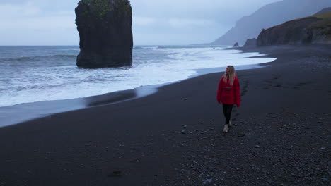 Female-Tourist-In-Red-Jacket-Walking-On-Black-Sand-At-Laekjavik-Beach-In-Iceland