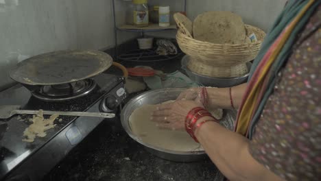 side angle close-up shot of a senior aged woman making traditional bhakri in indian kitchen using cooking gas stove