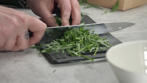 Close-up-camera-slowly-orbits-chef-chopping-arugula-on-cutting-board