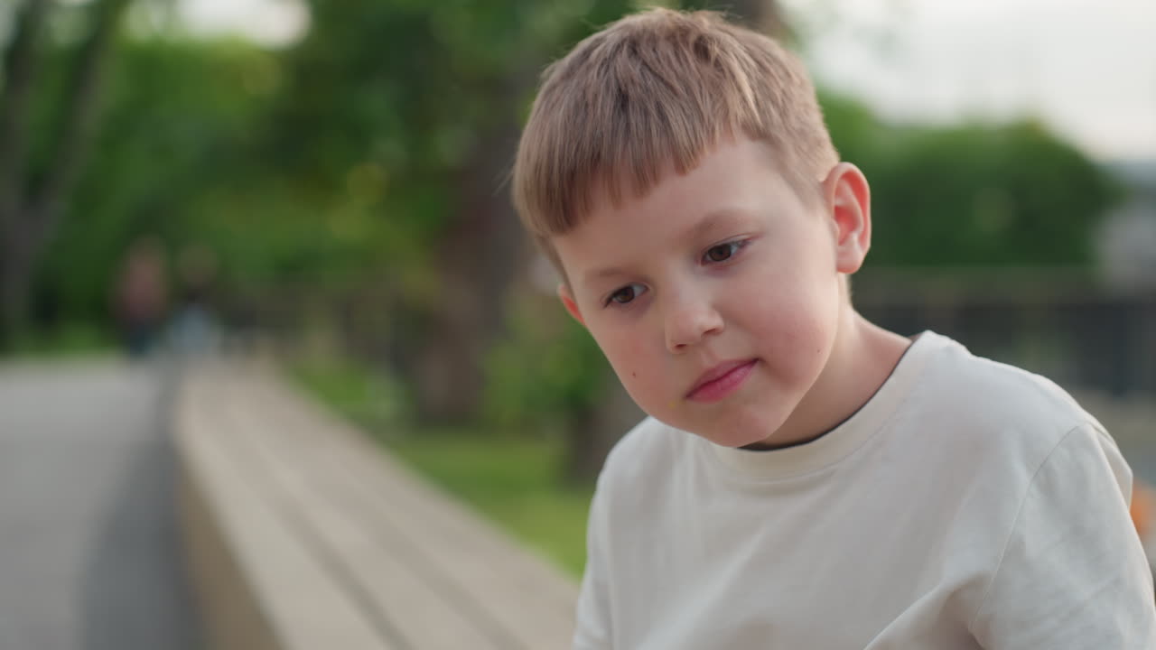 summer kid seated on wooden bench in park pondering drawing ideas on paper with pencil under warm summer light, thoughtful expression capturing creative moment as breeze rustles leaves around him