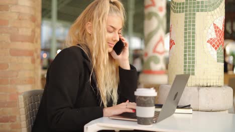 woman talking on smartphone while working with laptop in cafe