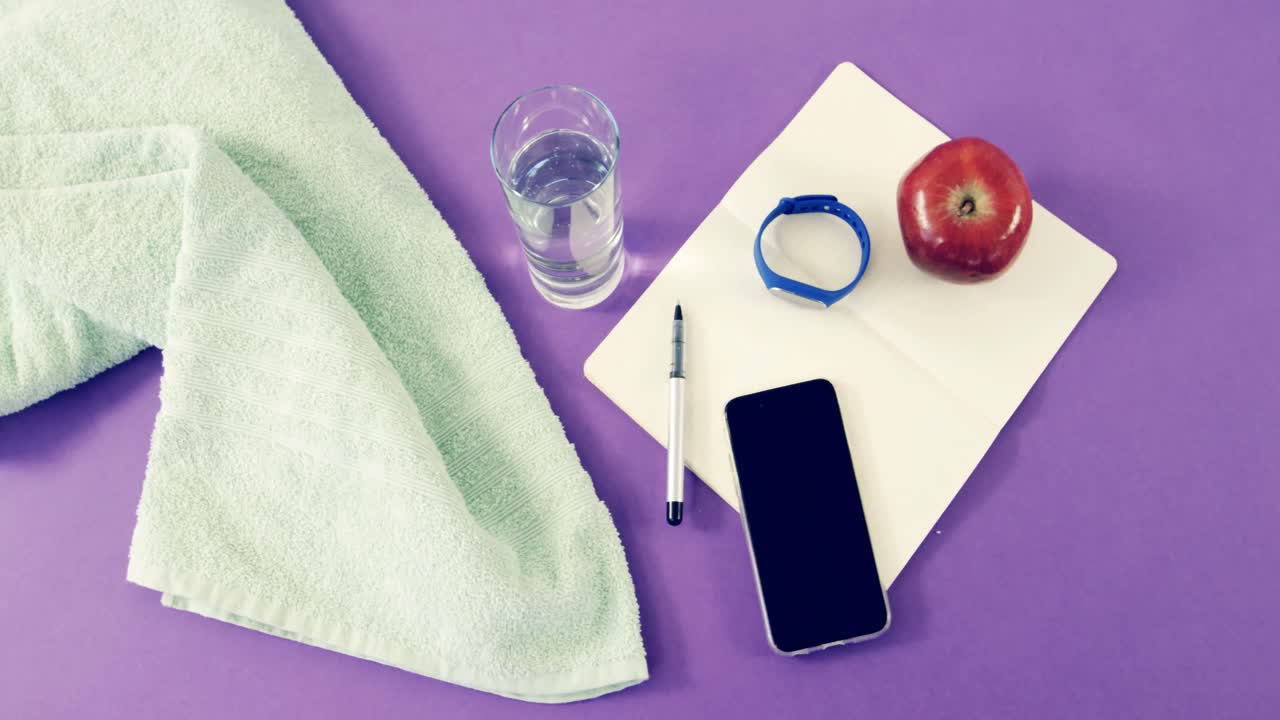 Telefono cellulare, tovagliolo, acqua, mela, taccuino, penna e fitness tracker