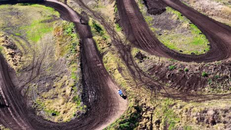 a dirt bike rider accelerates and jumps along a winding motocross track in a rural, sunlit australian bush setting, captured by aerial drone