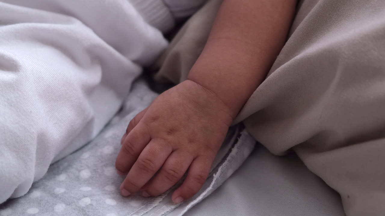 cerca de la mano y el brazo de un lindo bebé mientras duerme en la cama