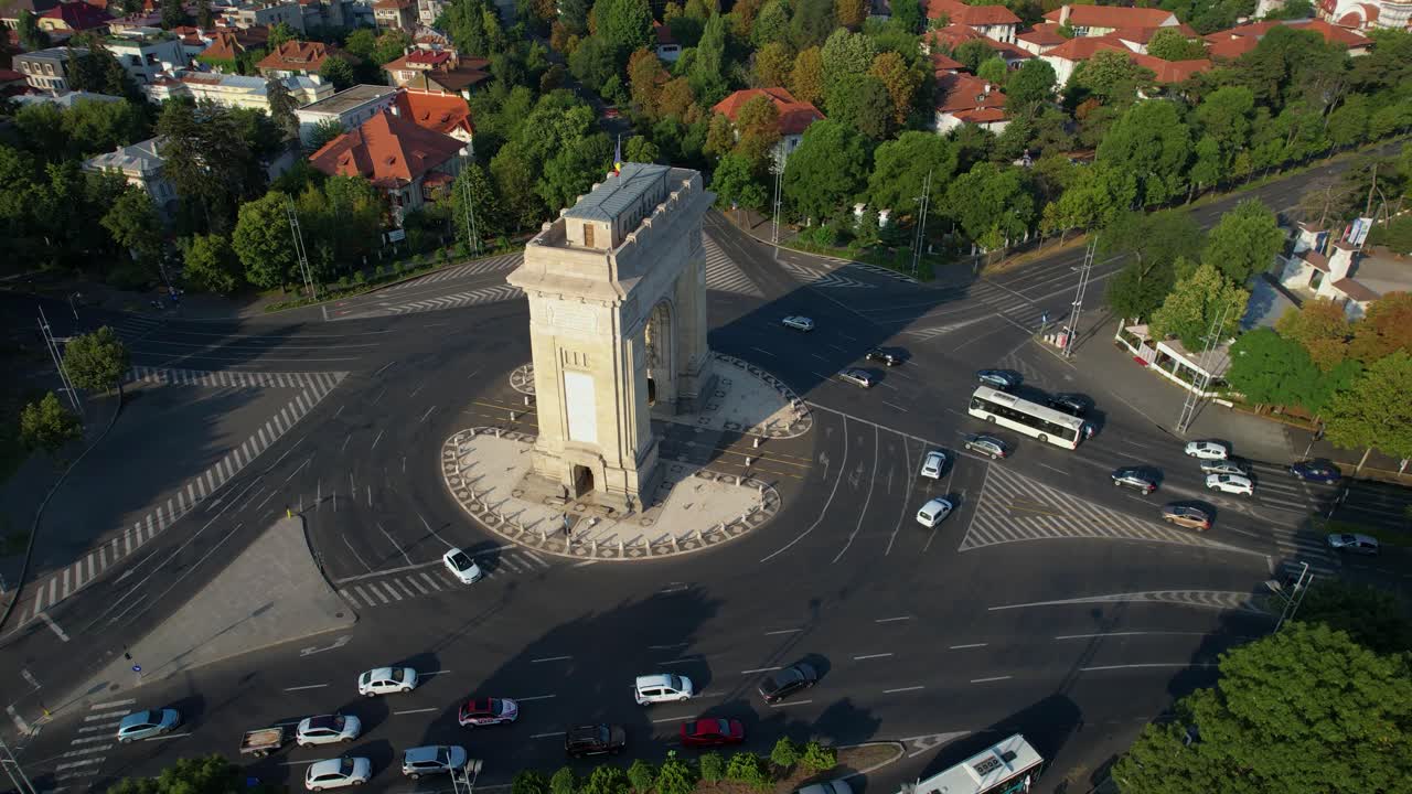 vista aérea giratoria sobre el arco del triunfo en bucarest, rumania, europa, amanecer, coches que pasan, arco del triunfo