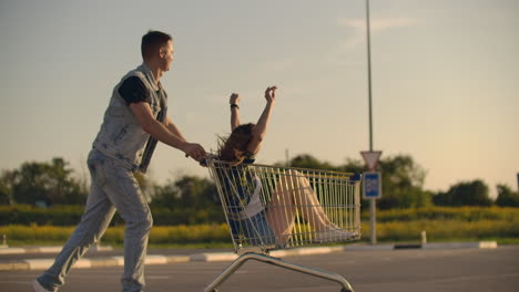 lens flare: cheerful people couple man and woman at sunset ride supermarket trolleys in slow motion.