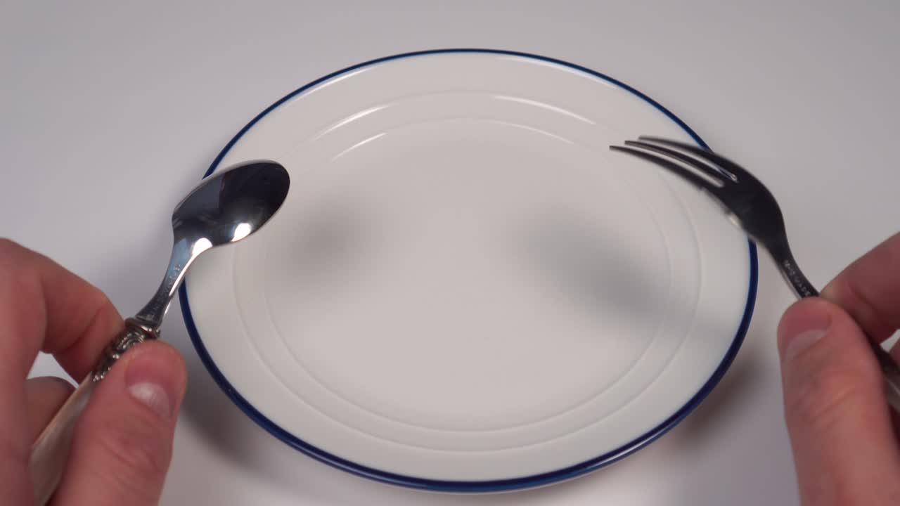 mpty white plate with a blue border on the table in a restaurant. In the hands of a dessert fork and spoon