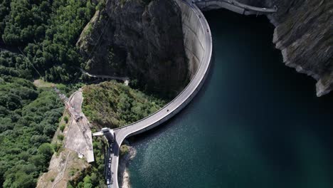 aerial shot of vidraru dam in romania, captured at an angle while circling left. blue lake, dramatic curves, and green mountain backdrop in 4k.