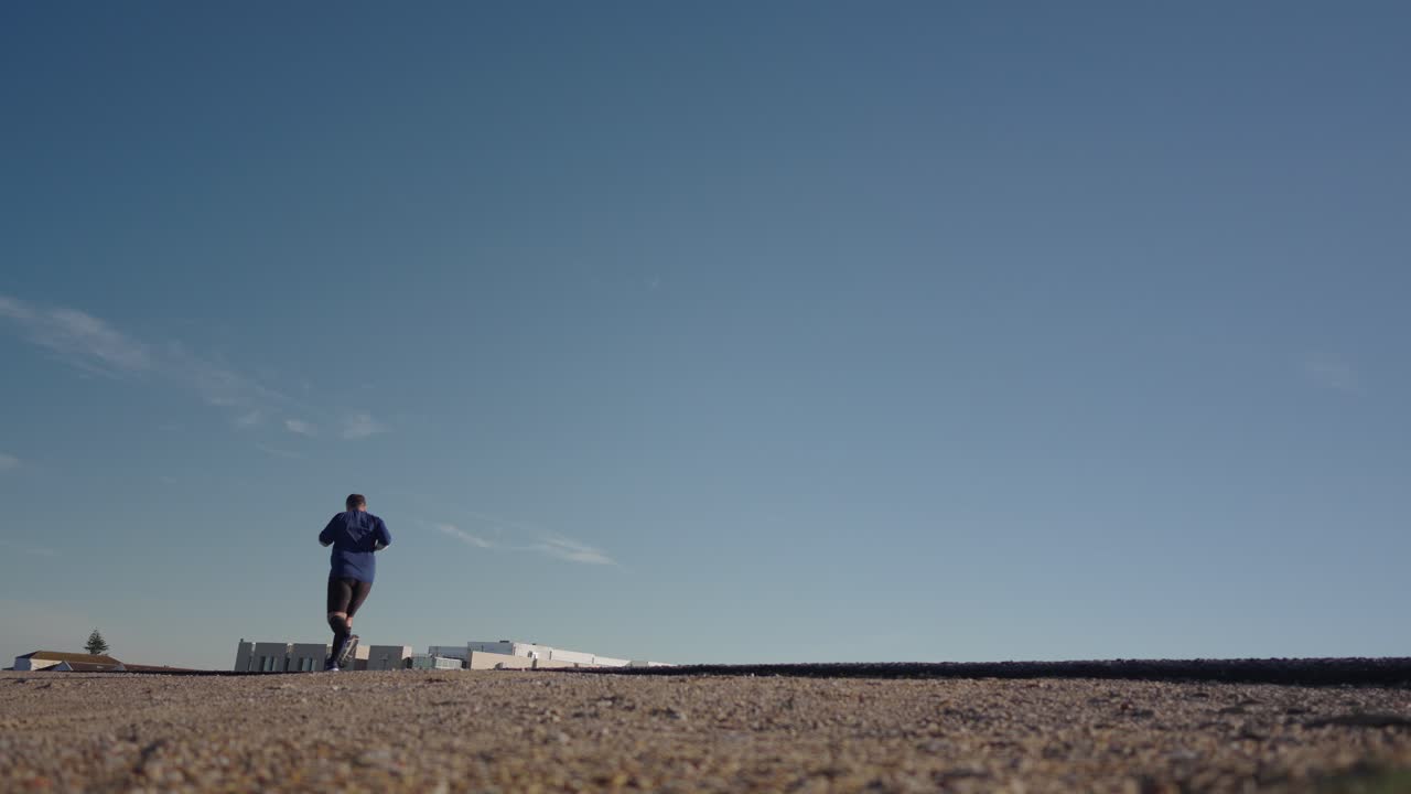 Runner running road, low angle back view, blue sky and empty roadway, healthy lifestyle