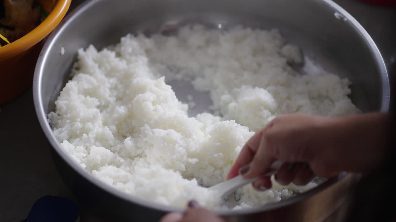 Close-up shot of a hand gently turning freshly cooked sushi rice in a metal pot