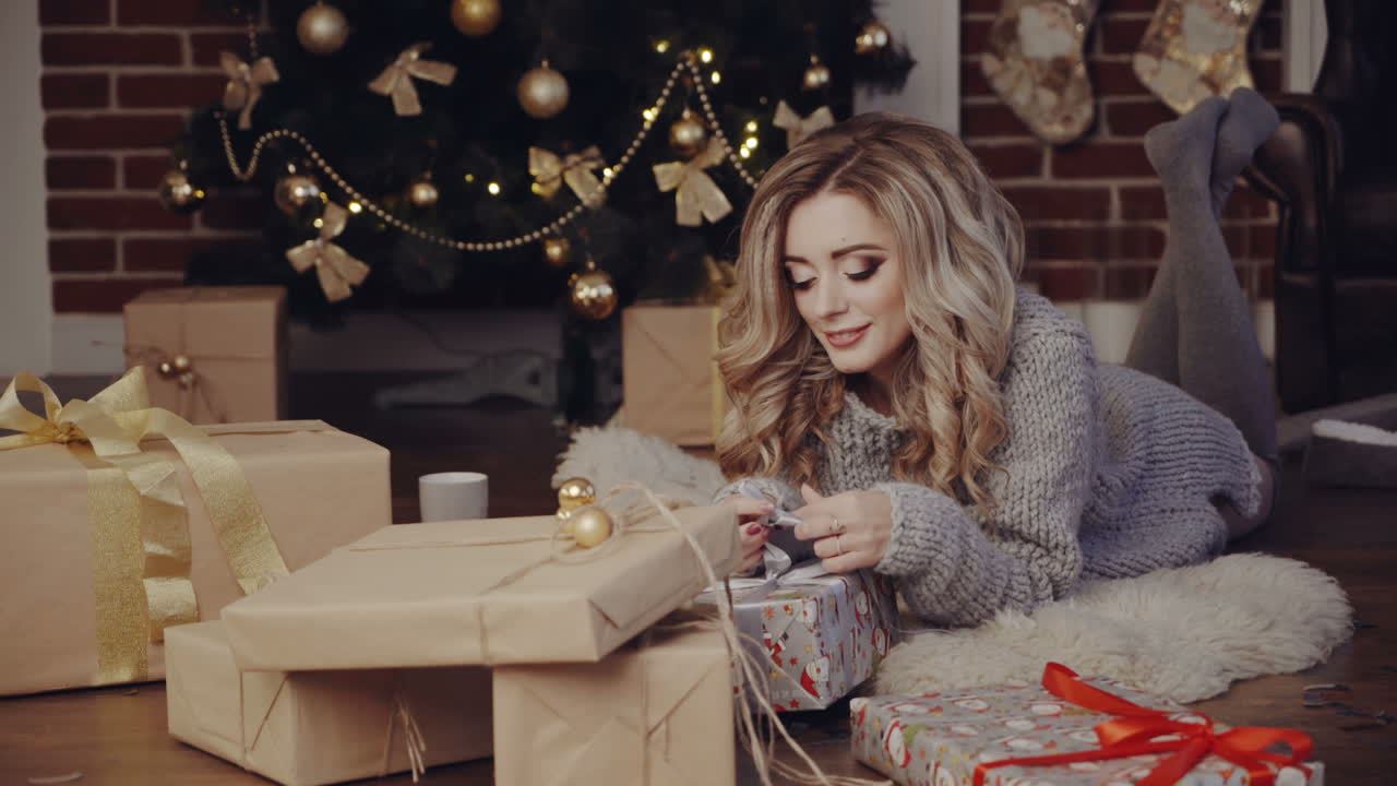 Woman opening gift boxes. Young woman with presents in New Year interior in the living room
