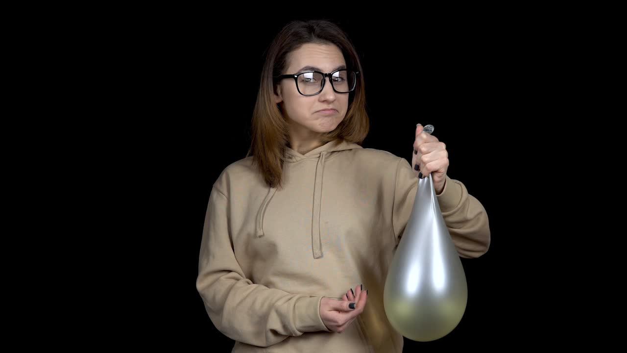 Young woman shakes balls with water. Girl shakes the ball on a black background. The balloon trembles like jelly.