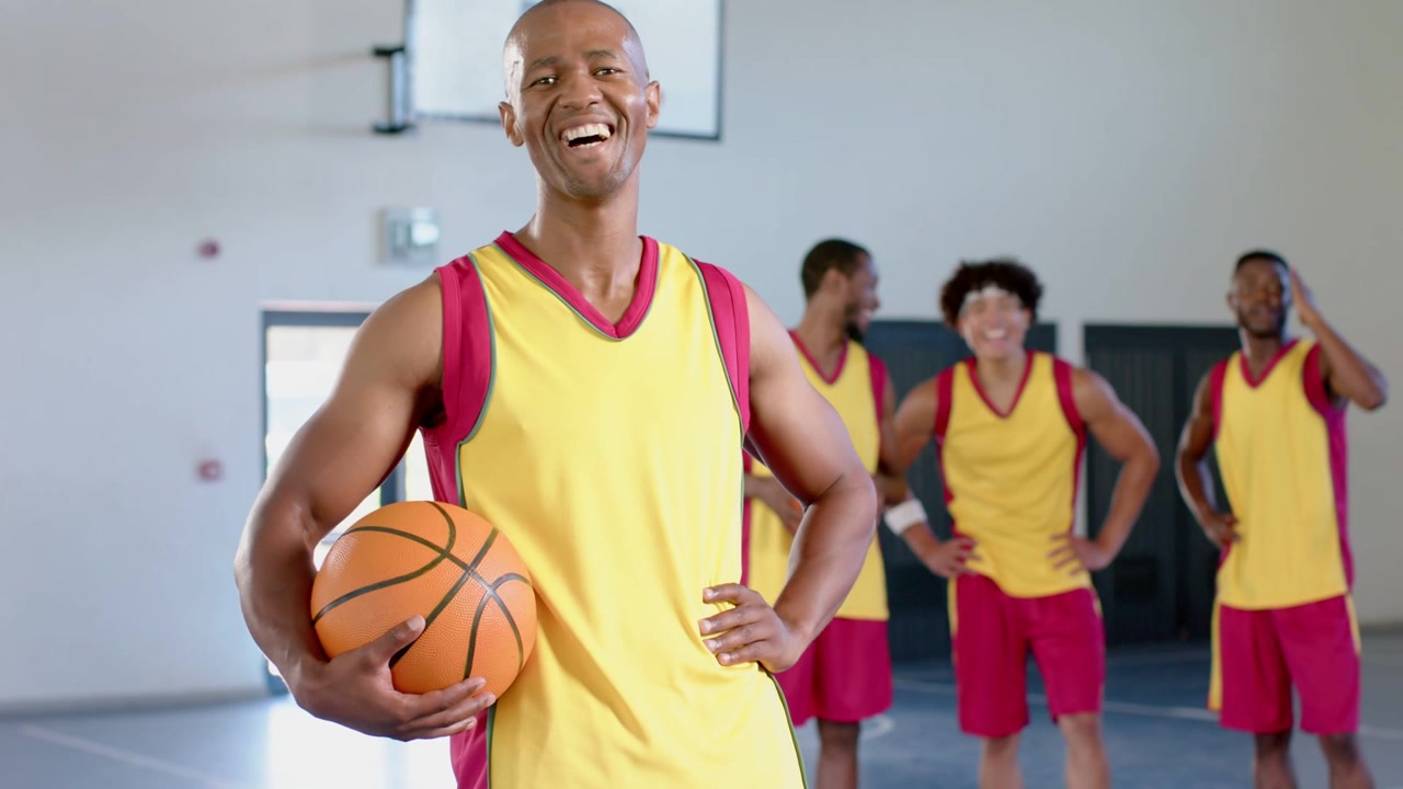 Jugador Masculino Sosteniendo Baloncesto Posando en Cancha de Gimnasio, con Insignias Sociales Deslizándose, Cubriendo el Torso