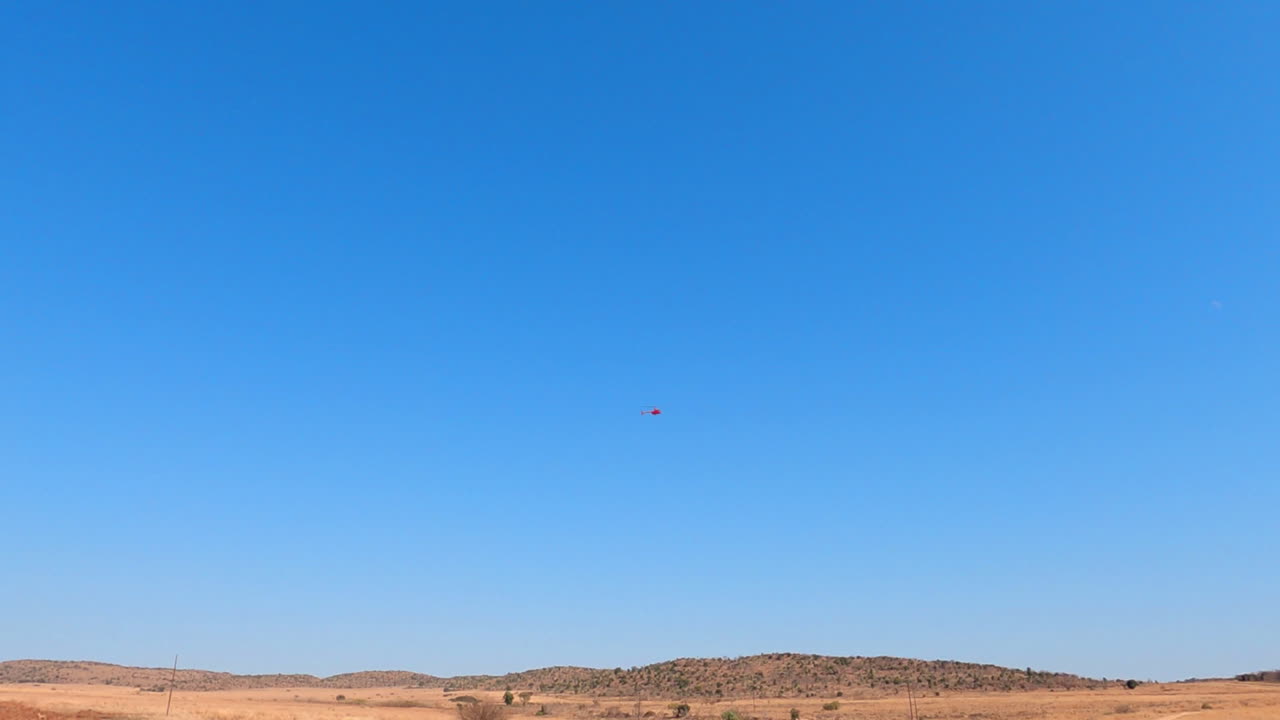 una amplia vista de un helicóptero rojo volando sobre un paisaje africano seco en una reserva de caza