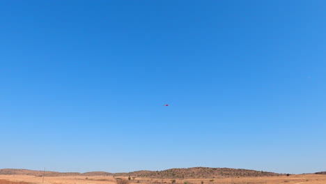 una amplia vista de un helicóptero rojo volando sobre un paisaje africano seco en una reserva de caza