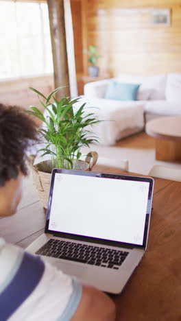 vertical video of african american man using laptop with copy space in log cabin