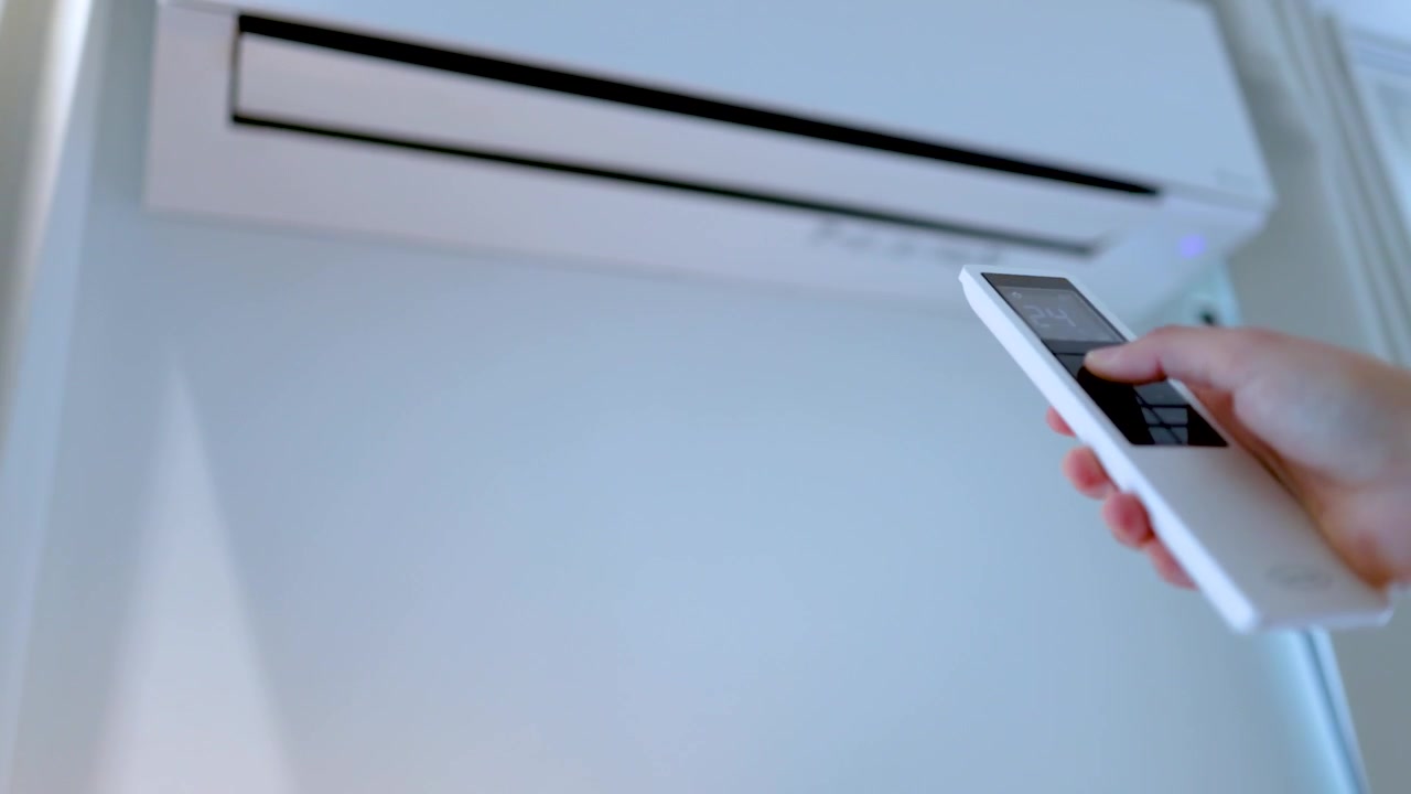 Een hand gebruikt een afstandsbediening om instellingen aan te passen op een witte binnenunit van een airco.