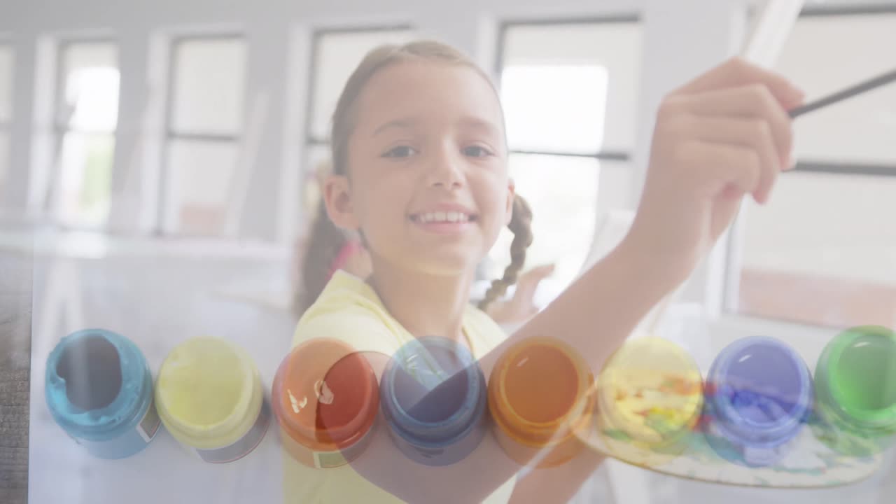 animación de ollas de pintura sobre una estudiante caucásica sonriente pintando en clase de arte
