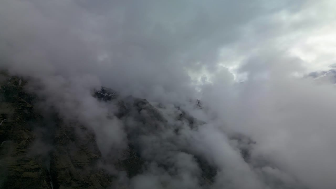 Thick mist and clouds drifting over rugged rocky slopes and snow-covered peaks in the Annapurna region, revealing dramatic Himalayan scenery and serene wilderness under a bright blue sky