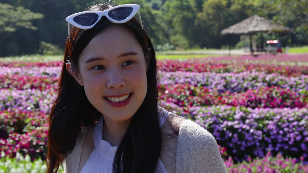 Cheerful woman strolls along floral path in sunny garden, camera slowly moving closer