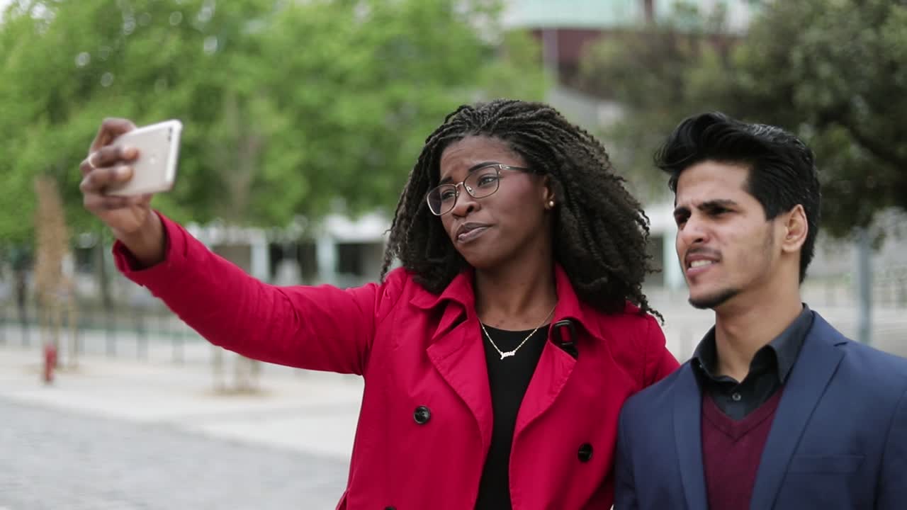 Woman and man making selfie outside, man making faces, posing