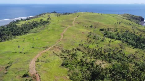 footpath trail on green rolling hill of corregidor island in siargao, aerial