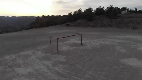 Aerial:-Orbit-shot-of-empty-football-goal-during-sunset-on-hard-pitch
