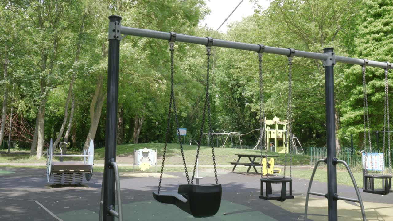 Empty swings in Hessle playground surrounded by trees on a calm sunny day