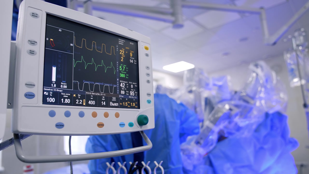 Segni vitali del paziente sul monitor della macchina per la ventilazione polmonare. Un chirurgo robotico esegue un'operazione sullo sfondo sfocato.