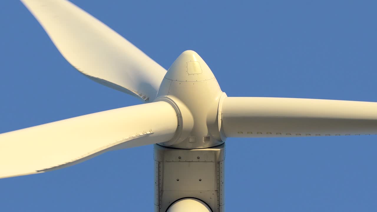 Nærbilde av en vindturbin som snurrer mot en klar blå himmel. Hvite blader genererer fornybar og bærekraftig energi i en moderne vindpark.