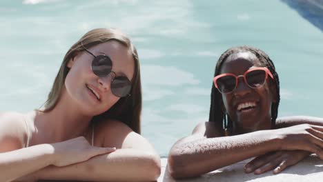 Portrait-of-happy-diverse-teenage-female-friends-in-sunglasses-smiling-in-swimming-pool,-slow-motion