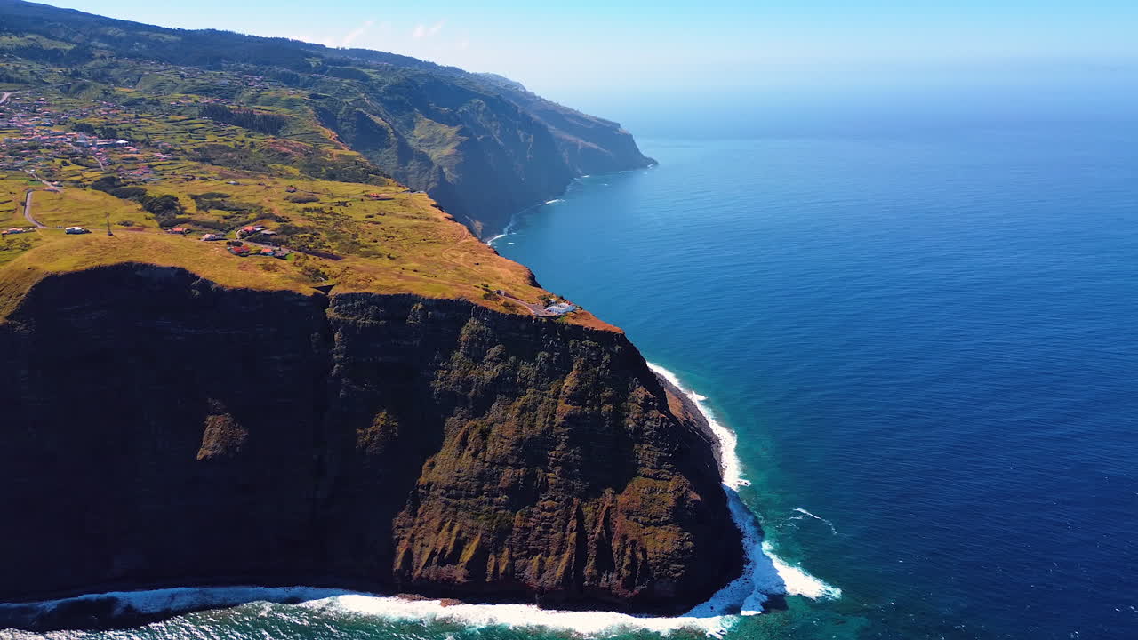 Residential area located on the high mountain at the coast of the Atlantic Ocean. Drone footage over the vast waterscape and the shore of the Madeira Islands, Portugal.