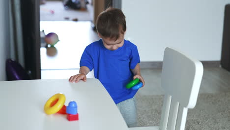 baby boy in blue t-shirt assembles toy pyramid. kid plays with a toy and drops it on the floor.