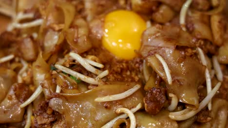 macro shots transition from a bowl of fried noodles with raw egg yolk to a plate of crispy turnip cake, under bright, even lighting and shallow depth of field