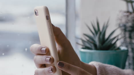 mano de mujer de cerca usando un teléfono inteligente navegando por mensajes en línea leyendo redes sociales disfrutando de la comunicación móvil de pie junto a la ventana relajándose en casa en un día frío y lluvioso