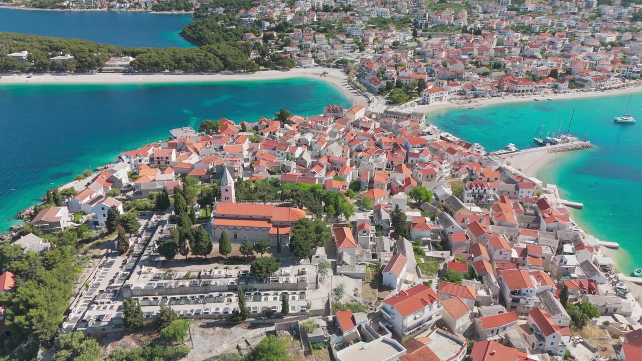 Dron se blíží k historickému městu Primošten na kopci od moře, stoupá nad kostelem a těsně krouží kolem věže a hřbitova s výhledem na Jadran