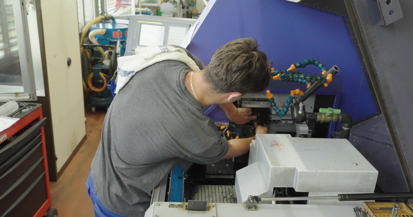 Operaio di fabbrica che aziona una macchina CNC a mani nude vicino a macchinari in movimento, illustrando i rischi per la sicurezza sul lavoro, la mancanza di dispositivi di protezione e la prevenzione degli incidenti industriali