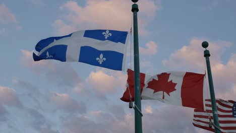 flags of quebec, canada, and america waving against cloudy sunset sky in magog, canada