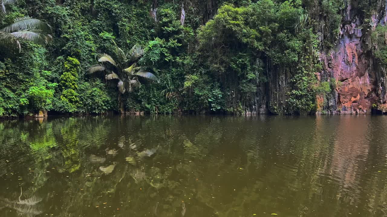 A Serene Lake Surrounded by Limestone Formations Draped in Trees and Vines at Kek Look Tong Cave in Ipoh, Malaysia - Pan Right Shot