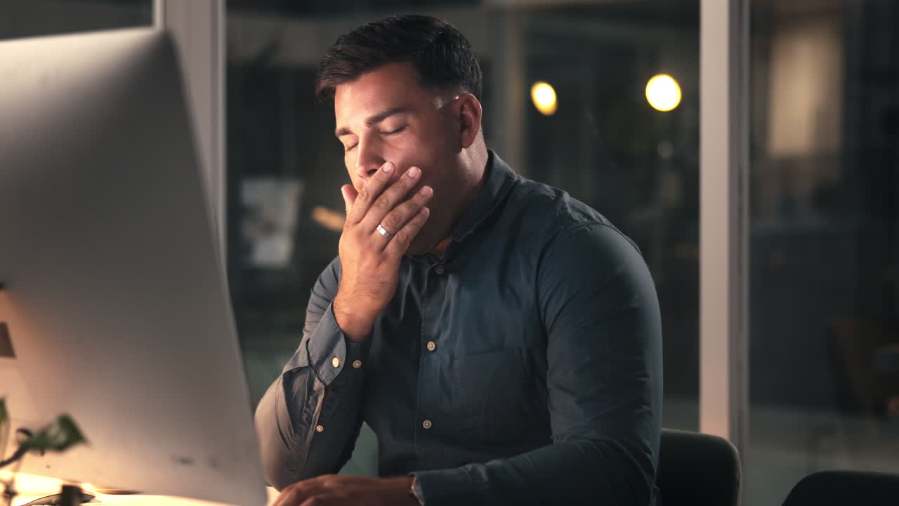 Man Yawning While Working Late on Computer in Office
