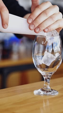 transparent glass with ice cubes. bartender is putting crystal ice cubes in a glass before preparing an alcoholic cocktail to customers on the bar table. vertical video