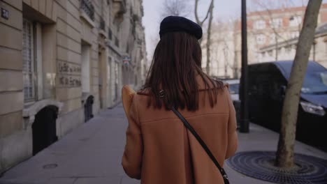 camera follows beautiful elegant happy woman walking along paris street with paper shoppping food bag slow motion.