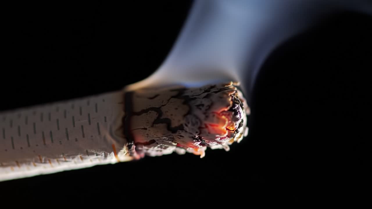 Close-up View of a Burning Cigarette in Dark Background Showcasing Ash and Smoke Details