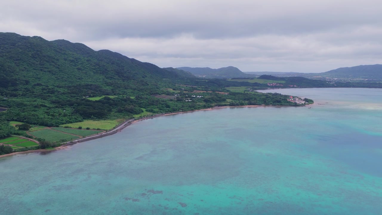 Japonya, Okinawa, Ishigaki Adası'ndaki Nagura Koyu'nun turkuaz suları, kıyı şeridi ve ormanlık tepelerinin üzerinde yukarı doğru yükselen yatay havadan çekim
