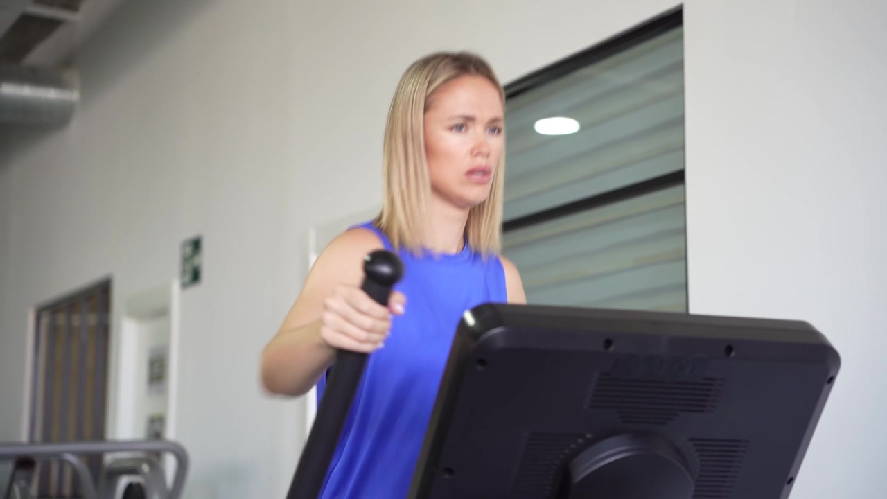Una donna si allena su un'ellittica in palestra, concentrata e determinata nel suo allenamento.