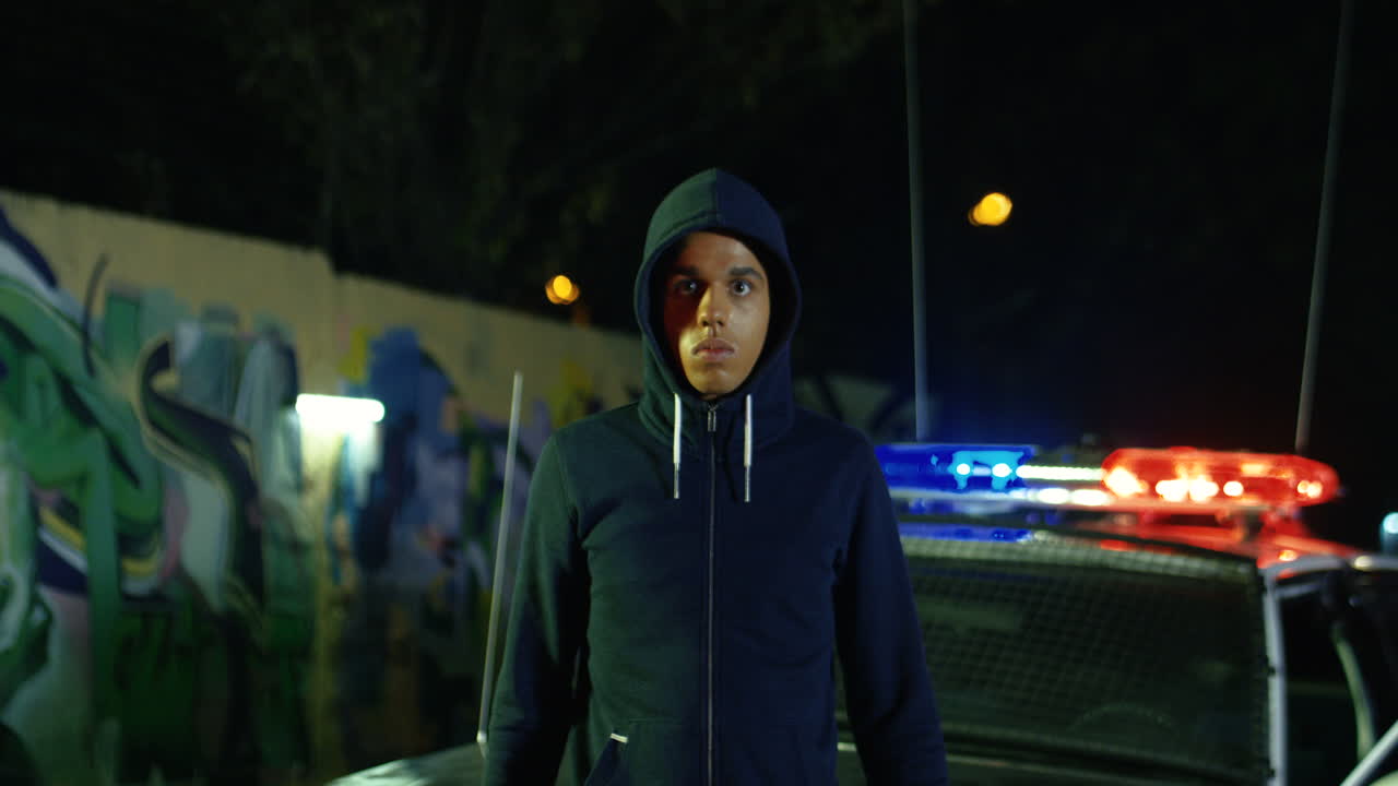 똑바로 보고 카메라에 총을 가리키는 후드에 젊은 물라토 남성 범죄자의 초상화 샷