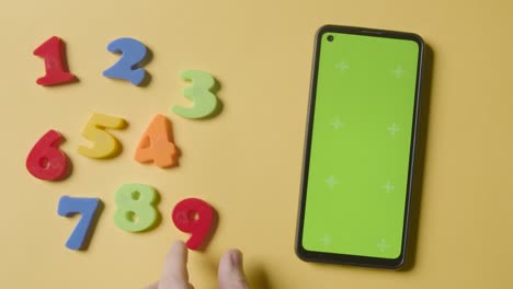 studio overhead shot of plastic numbers arranged in order with green screen mobile phone on yellow background