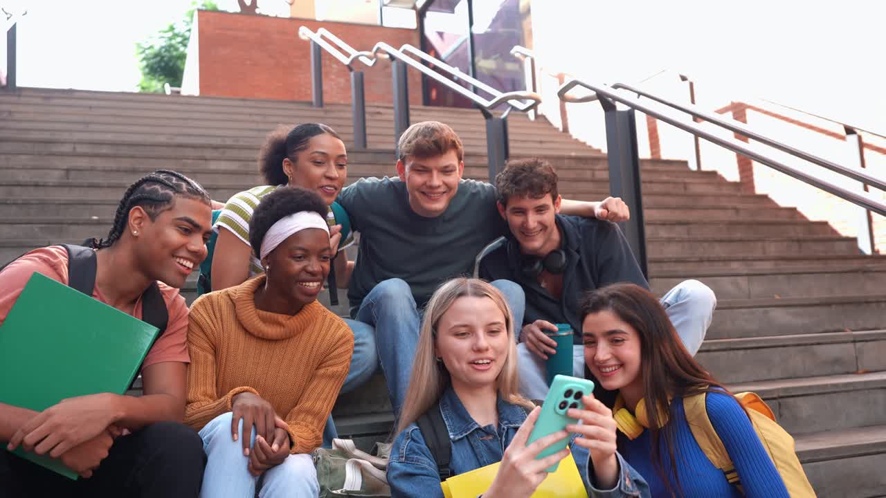 Studenti multietnici felici che usano lo smartphone insieme sui gradini del campus