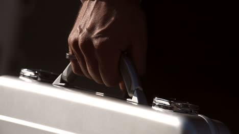 close up of a man's hand holding a silver briefcase carrying valuables standing outside in the city centre